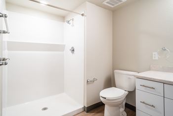 A white bathroom with a toilet, sink, and shower. at All Saints Apartments, DENVER, CO